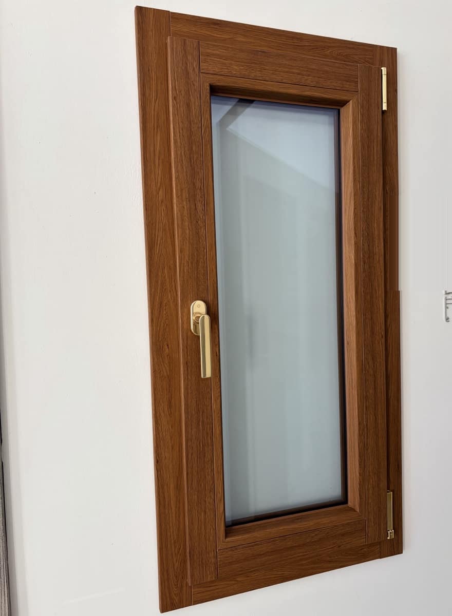 Finestra in PVC con finitura effetto legno e maniglia dorata, esposta nello showroom Infiss.Art di Terni